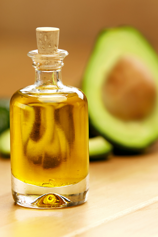 Avocado oil in a bottle and cut avocado in the background