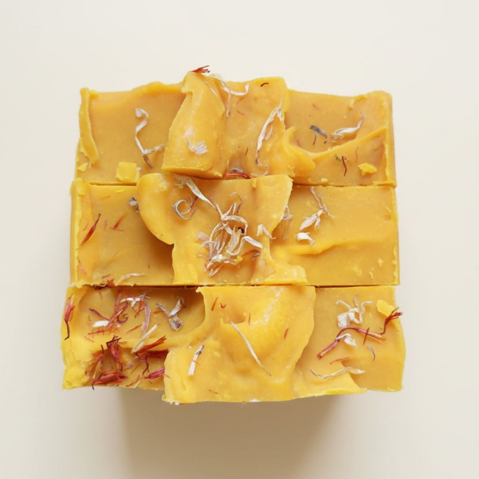 Yellow soap bar with visible herbs on a light beige background