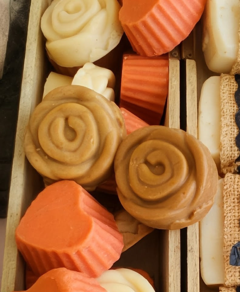 Assorted handmade soap bars with different shapes and colors in a wooden box.