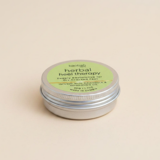 A silver metal tin of baobab Herbal Heel Therapy balm with a light green label, set against a solid beige background.