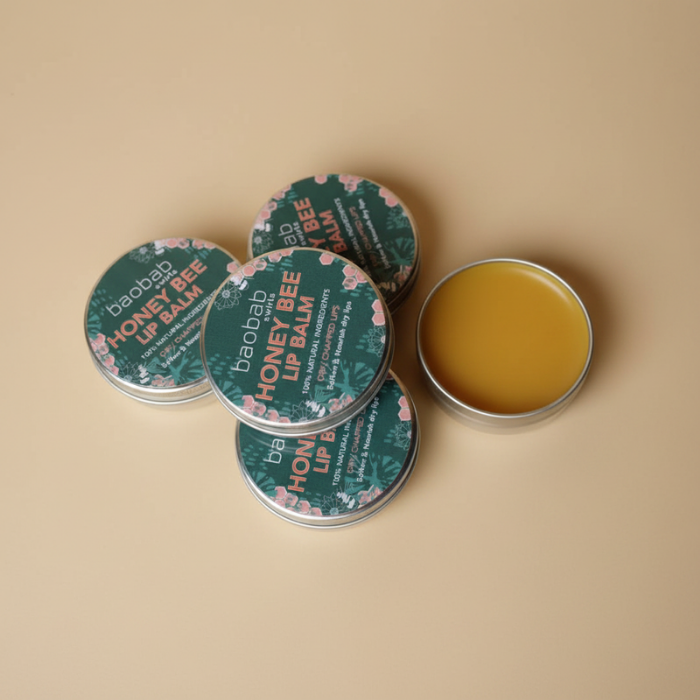 Four round metal tins of baobab swirls Honey Bee Lip Balm arranged on a warm beige background, with one tin open to show the golden-yellow balm inside.