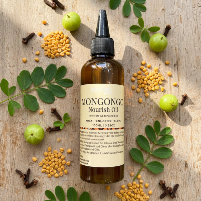 Bottle of Baobab Swirls Mongongo Nourish Oil surrounded by green amla, leaves, and seeds on a wooden surface