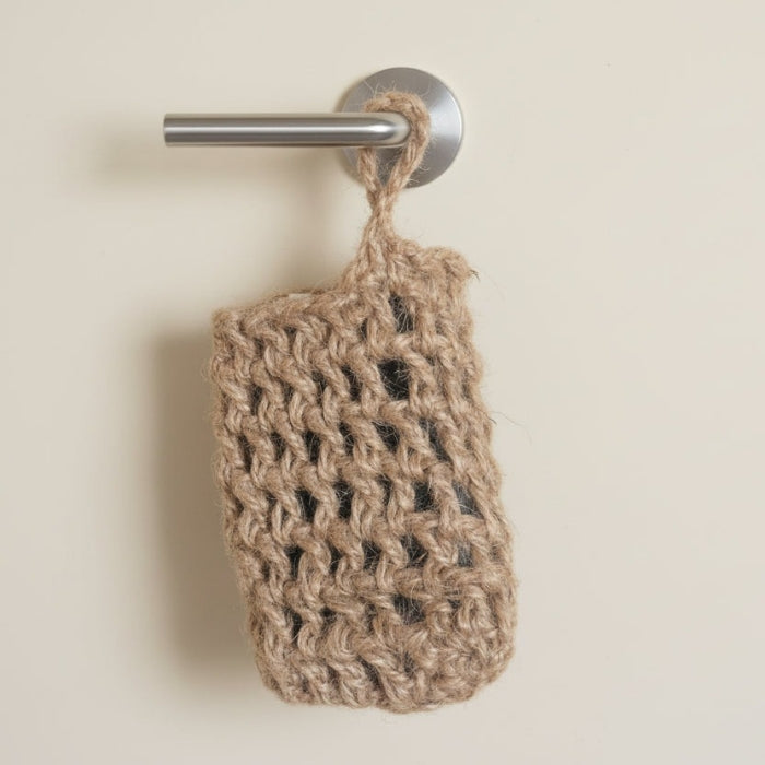 Brown woven soap saver hanging on a silver towel hook against a beige wall.