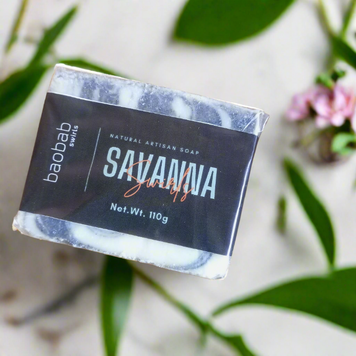Bar of Baobab Swirls Savanna soap with a black label on a light background with green leaves.