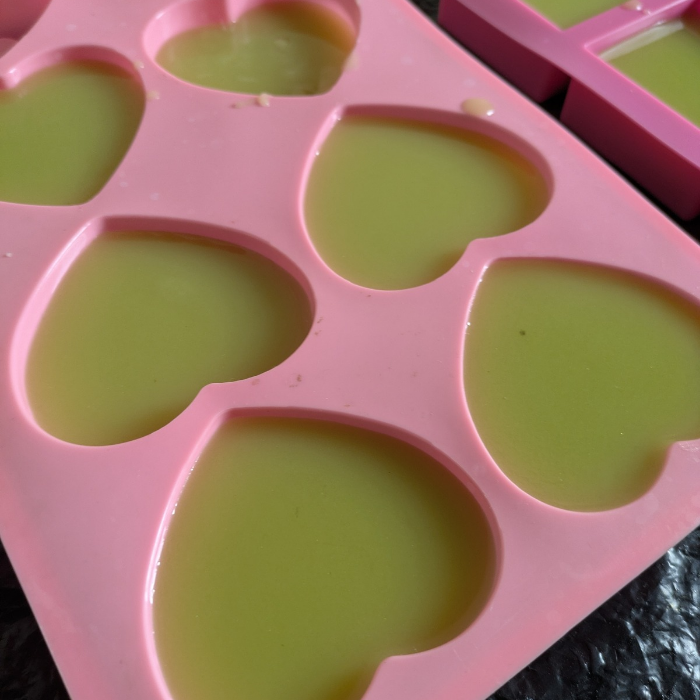Pink silicone mold with heart-shaped cavities containing  wet soap.