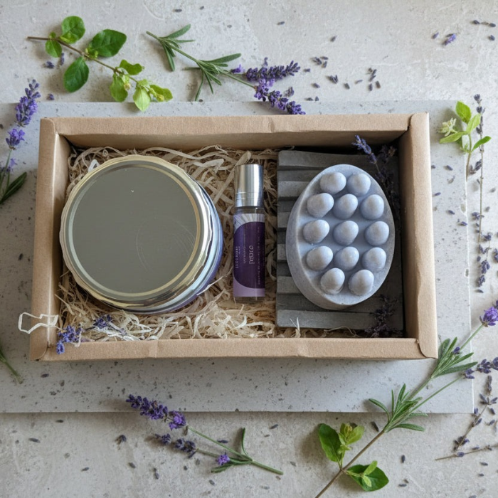 Box containing a roller bottle ,body cream and soap with lavender and greenery around.